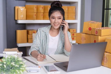 Genç kadın girişimci müşteri ile cep telefonu ve yazma ürün siparişinde evde ofis konuşuyor.