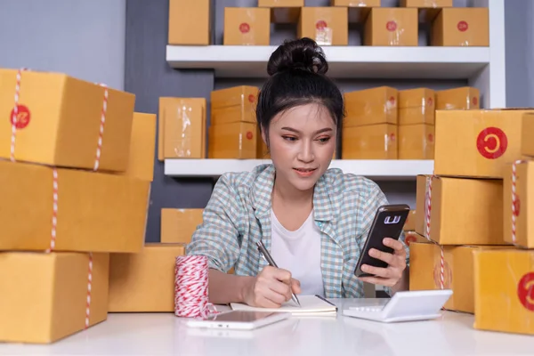 young woman entrepreneur checking and writting order with cardboard , SME business online prepare for delivery to customers in home office