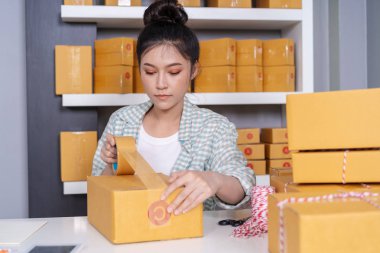 Genç kadın online girişimci parsel ambalaj için bant kullanarak evde ofis kutusuna, ürün müşteriye teslim için hazır olun.