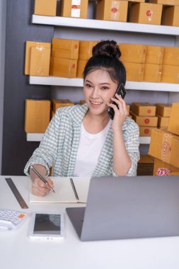 Genç kadın girişimci müşteri ile cep telefonu ve yazma ürün siparişinde evde ofis konuşuyor.