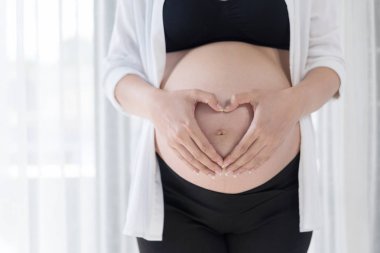 hamile kadının göbek üzerinde kalp şeklinde el ele tutuşarak kapatın