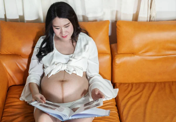 Mulher grávida olhando ultra-som álbum de fotos na sala de estar — Fotografia de Stock