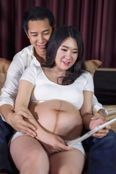 Terhes nő férje segítségével digitális tábla ágyon — Stock Fotó