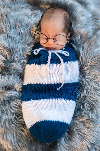Newborn baby boy wearing glasses sleeping and swaddled in a knit — Stock Photo, Image