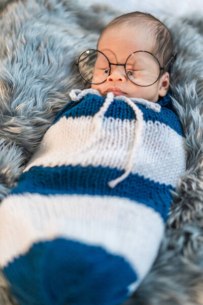 newborn baby boy wearing glasses sleeping and swaddled in a knit