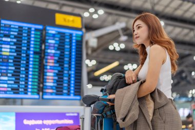 Havaalanında bilgi panosuyla uçuş bekleyen bir kadın.