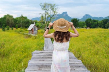 woman wearing hat and standing on wooden bridge with cosmos flow