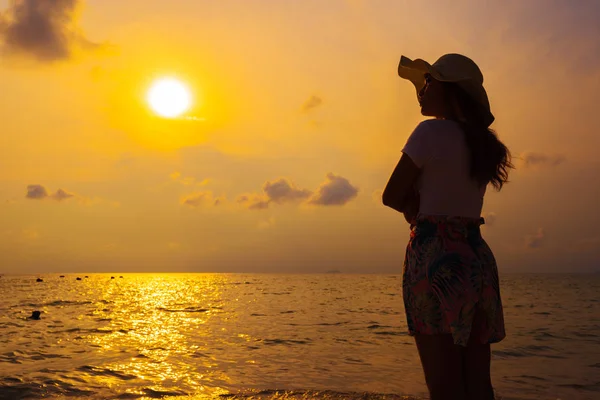 Mujer con sombrero de pie en la playa al atardecer — Foto de Stock