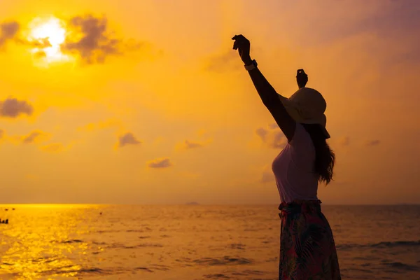 Mujer con sombrero con los brazos levantados de pie en la playa del mar en los soles — Foto de Stock