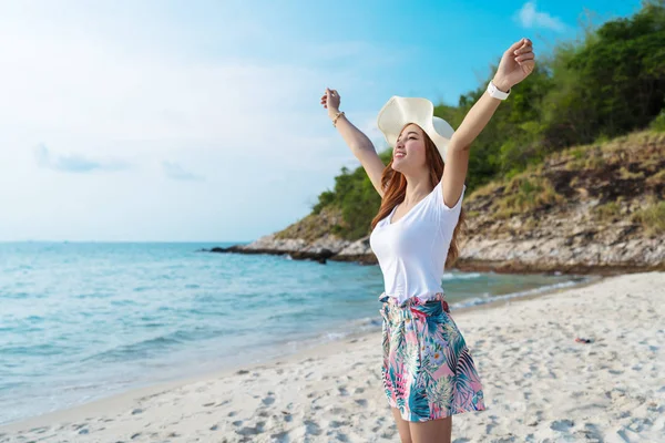 Kvinna bär hatt med armar upp stående på havet stranden — Stockfoto