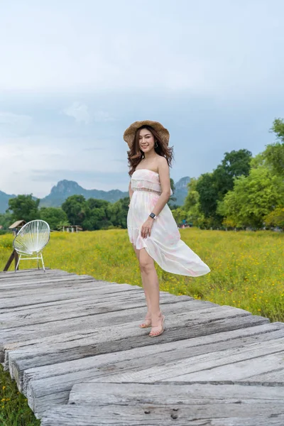 Mulher feliz de pé na ponte de madeira com flor cosmos amarelo — Fotografia de Stock