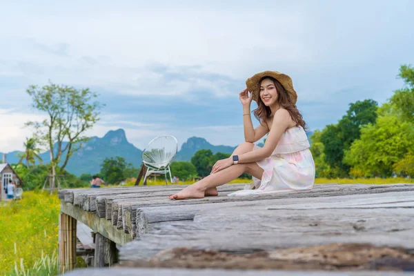Donna seduta su un ponte di legno con campo di fiori cosmo giallo — Foto Stock