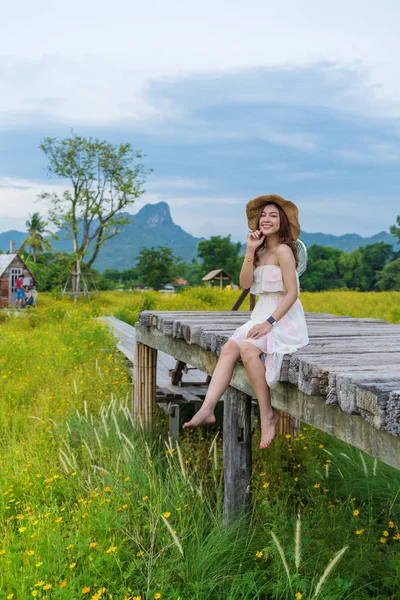 Mujer sentada en puente de madera con campo de flores cosmos amarillo —  Fotos de Stock