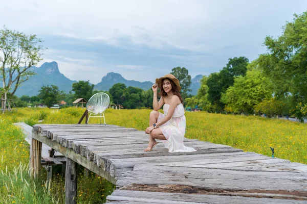 Woman sitting on wooden bridge with yellow cosmos flower field — Stock Photo, Image