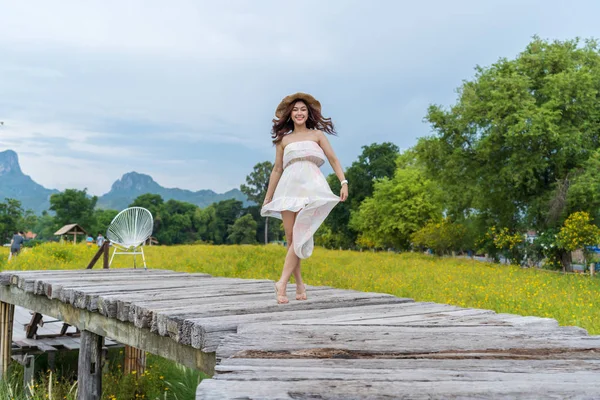 Mulher feliz de pé na ponte de madeira com flor cosmos amarelo — Fotografia de Stock