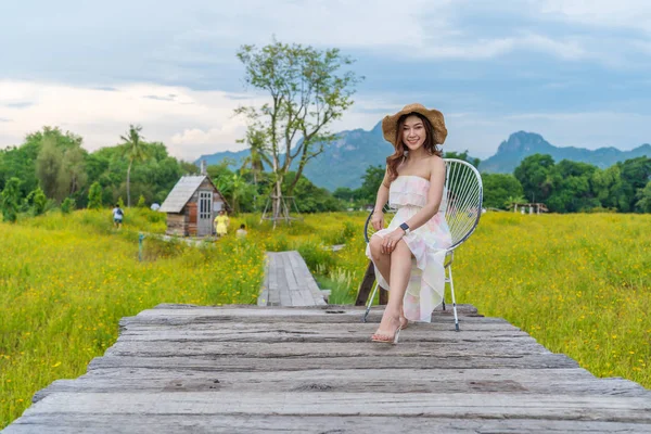 Woman sitting on wooden bridge with yellow cosmos flower field — Stock Photo, Image