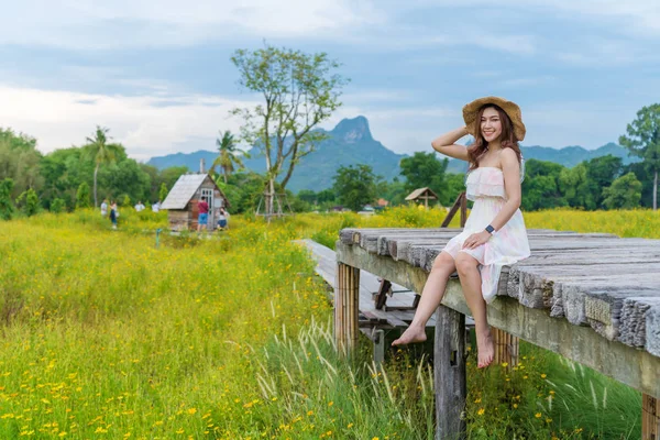 Mujer sentada en puente de madera con campo de flores cosmos amarillo —  Fotos de Stock