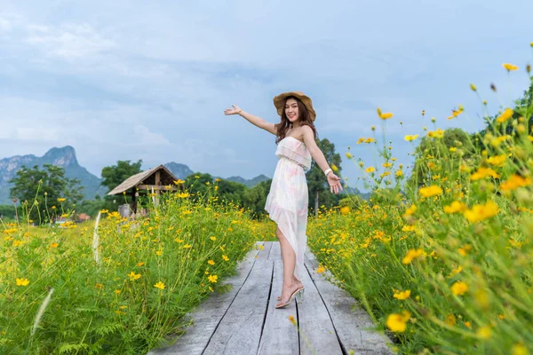 Woman with arm raised on wooden bridge with yellow cosmos flower — Stock Photo, Image