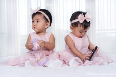 yatakta pembe elbise iki ikiz bebekler, bir oyun akıllı telefon
