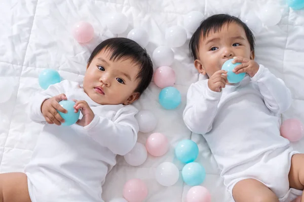 Cheerful twin babies playing color ball on bed — Stock Photo, Image