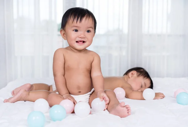 Дети-близнецы на кровати, один играет цветной мяч, один спит — стоковое фото