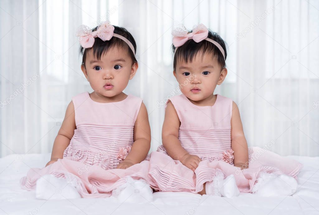 Two twin babies in pink dress on a bed