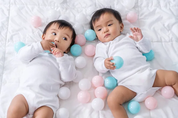 Cheerful twin babies playing color ball on bed — Stock Photo, Image