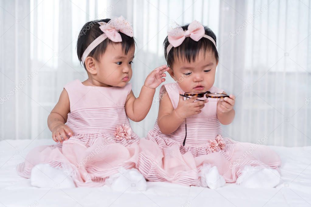 Two twin babies in pink dress on a bed