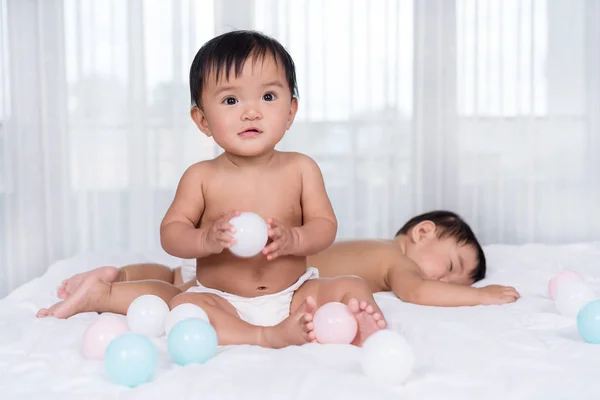 Bambini gemelli sul letto, uno che gioca a palla a colori, uno che dorme — Foto Stock