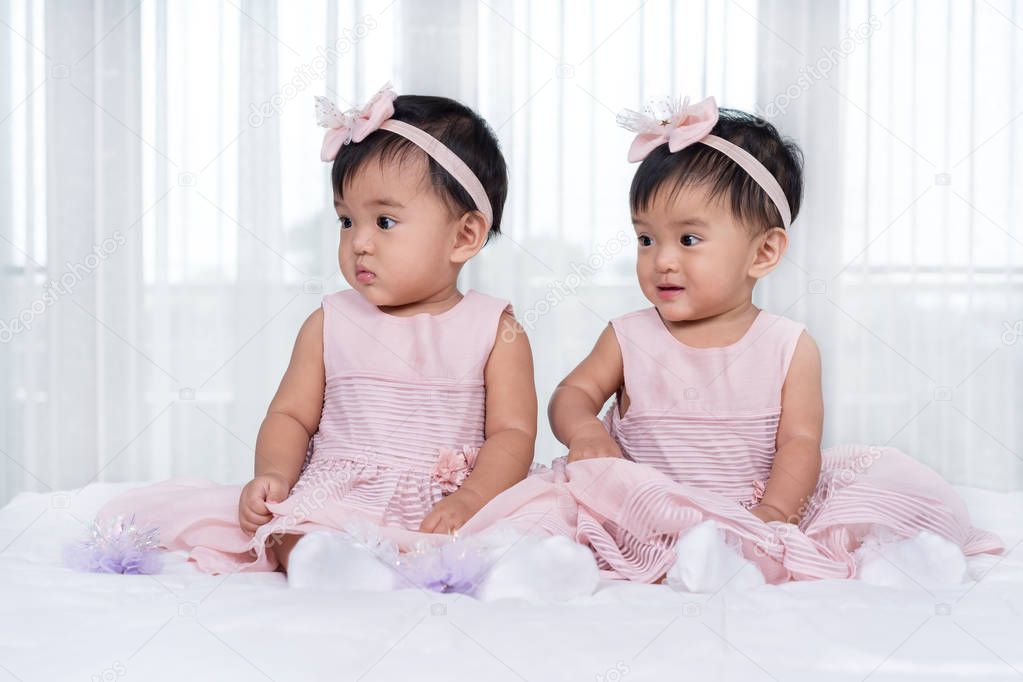 two twin babies in pink dress on bed