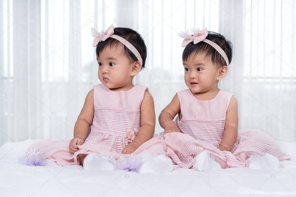 Two twin babies in pink dress on a bed