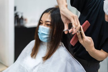 Kuaför kadın bir müşteriye saç kesiyor, insanlar koronavirüsü (covid-19) korumak için tıbbi maske takıyor olmalılar. yeni normal kavramlar