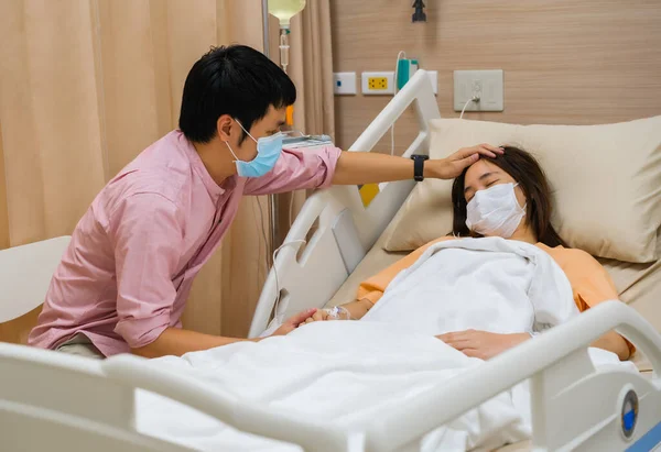 男人在医院的床上拜访和照顾女病人 人们必须戴上医疗面罩以预防大脑皮层病毒 Covid 的流行 — 图库照片