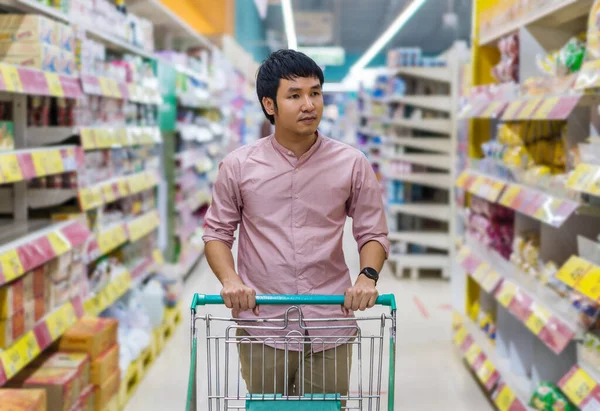 young asian man with shopping cart in supermarket department store