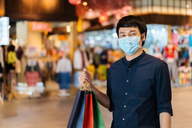 Genç Asyalı adam alışveriş merkezinde çanta ve Coronavirus (Covid-19) salgınını önlemek için tıbbi maske takıyor. yeni normal kavramlar