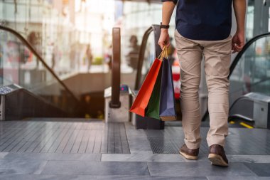 Alışveriş merkezinde yürürken alışveriş torbaları taşıyan genç adamın bacağını kapat.