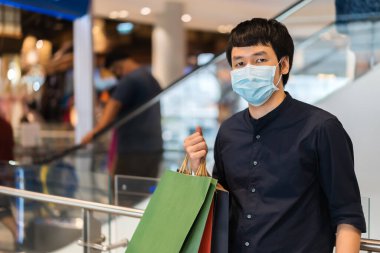 Genç Asyalı adam alışveriş merkezinde çanta ve Coronavirus (Covid-19) salgınını önlemek için tıbbi maske takıyor. yeni normal kavramlar