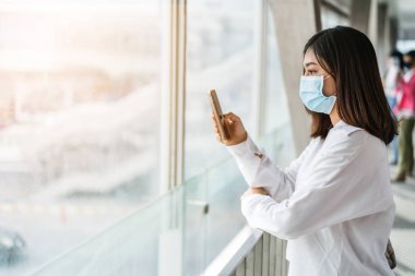 Genç Asyalı kadın şehirde koronavirüs (Covid-19) salgınını önlemek için akıllı telefon kullanıyor ve tıbbi maske takıyor. yeni normal kavramlar