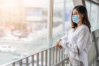 Kentte Coronavirus (Covid-19) salgınını önlemek için tıbbi maske takan genç Asyalı kadın görülüyor. yeni normal kavramlar