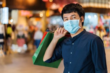Genç Asyalı adam alışveriş merkezinde çanta ve Coronavirus (Covid-19) salgınını önlemek için tıbbi maske takıyor. yeni normal kavramlar