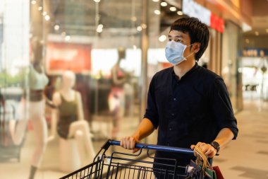 Alışveriş arabalı genç bir Asyalı ve Coronavirus (covid-19) salgınını önlemek için tıbbi maske takıyor. yeni normal kavram