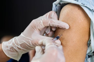 Doktor eldiven giyip hastaya şırınga enjekte edecek. Covid-19 veya koronavirüs aşısı