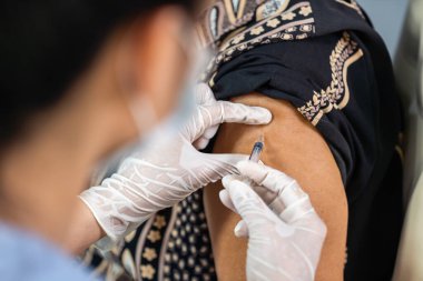 Doktor eldiven giyip elinde şırıngayla hastaya tıbbi maske takıyor. Covid-19 veya koronavirüs aşısı