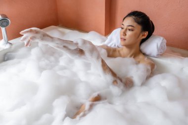 Genç kadın rahatlıyor ve köpükle banyo yapıyor.