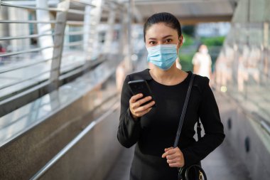 Şehirdeki Coronavirus (covid-19) salgınından korunmak için akıllı telefon kullanan ve tıbbi maske takan bir iş kadını