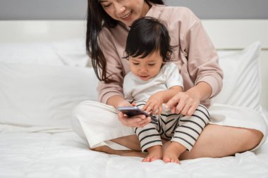 Bebekle anne yatakta akıllı telefon kullanıyor.