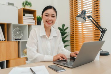 Ofiste dizüstü bilgisayarla çalışan mutlu genç bir kadın.