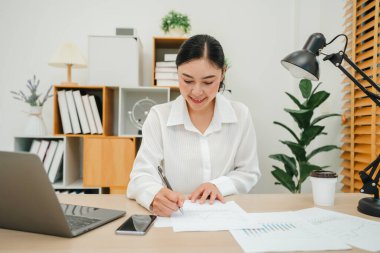 Mutlu bir kadın ev ofisindeki bilgisayarla tutarlı ya da evrak işleriyle uğraşıyor.