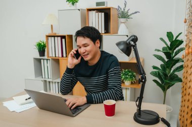 Ofiste bilgisayarla çalışırken akıllı telefonla konuşan mutlu bir adam.