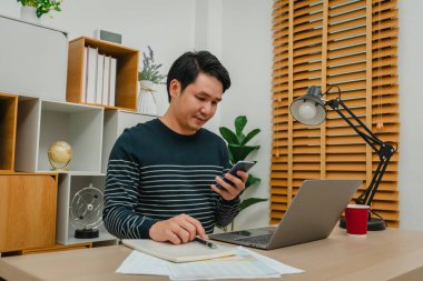 Ofiste akıllı telefon ve dizüstü bilgisayarla çalışan genç adam